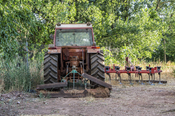 Alter rostiger Traktor auf einem Feld neben einigen Bäumen - Foto, Bild