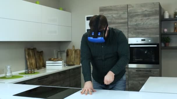 Fat man cooks through the virtual reality headset in kitchen simulation. Head-mounted display help a person cut with a knife. The male gamer plays with VR headset like he cooks. - Video