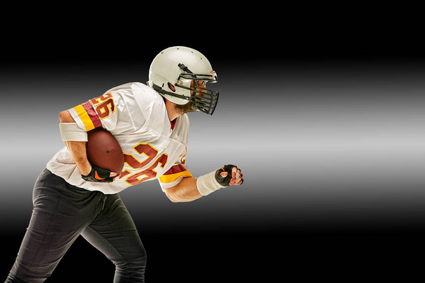 American football speler in beweging met de bal op een zwarte achtergrond met een lichte lijn, kopieer ruimte. Het concept van het spel is Amerikaans voetbal, beweging. Zwart witte achtergrond, kopieer ruimte. sport - Foto, afbeelding