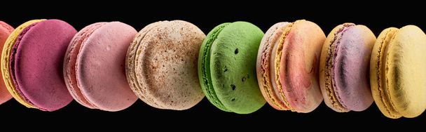 Reihe köstlicher farbenfroher französischer Makronen unterschiedlicher Geschmacksrichtungen isoliert auf schwarzem, panoramischem Foto - Foto, Bild
