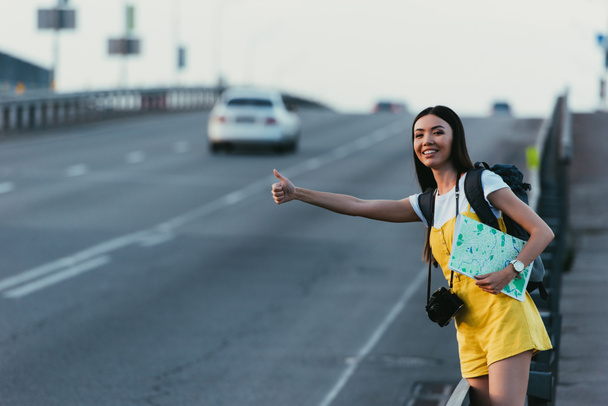 asian woman in yellow overalls hitchhiking and holding map - Photo, Image
