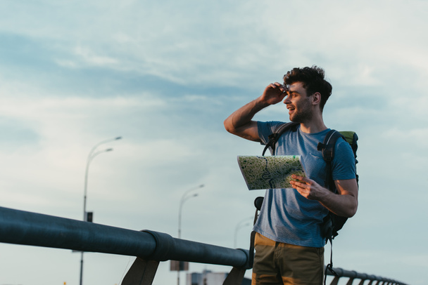 handsome man in t-shirt and shorts holding map and looking away  - Photo, Image