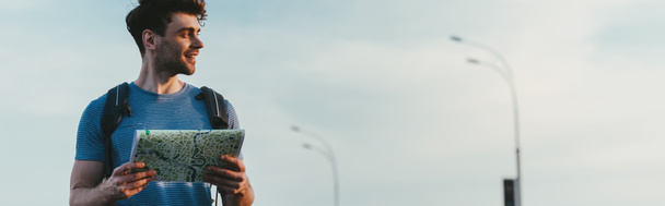 panoramische shot van glimlachend en knappe man in t-shirt Holding kaart  - Foto, afbeelding