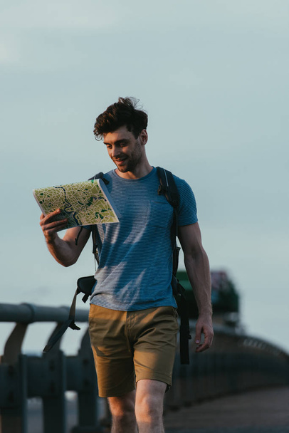 handsome man in t-shirt and shorts looking at map  - Foto, imagen