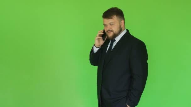Bearded fat businessman in black suit talking on phone. Green chromakey. Plump man solves problems by smartphone. Person discusses important issues - Felvétel, videó