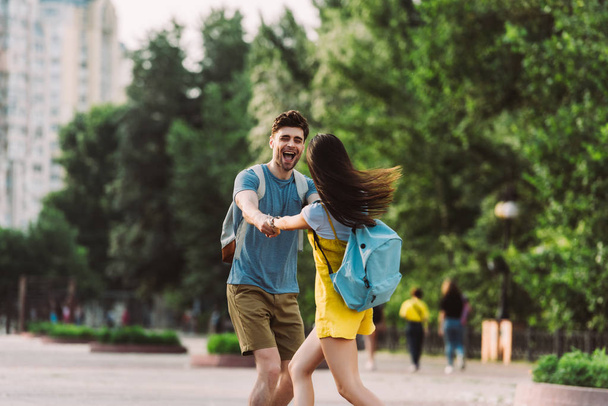Красивый мужчина и женщина с рюкзаками улыбаются и держатся за руки
  - Фото, изображение