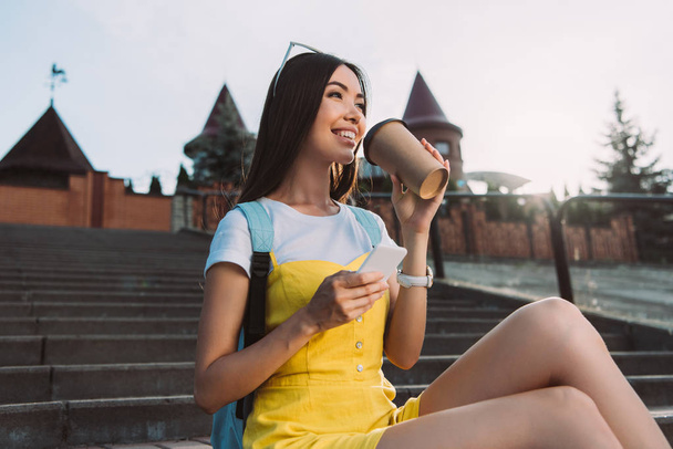 souriant et asiatique femme tenant smartphone et boire du café
  - Photo, image