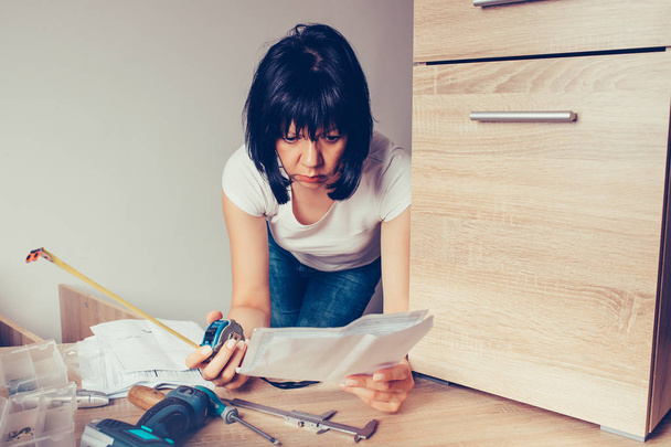 Женщина читает инструкцию по сборке мебели и использует м
 - Фото, изображение