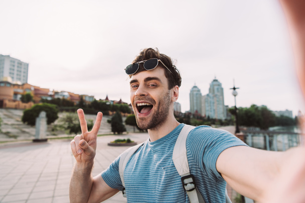 handsome man with glasses showing peace sign and taking selfie  - Photo, Image