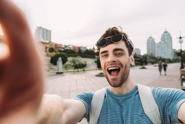 valikoiva painopiste komea mies lasit hymyillen ja ottaen selfie
  - Valokuva, kuva