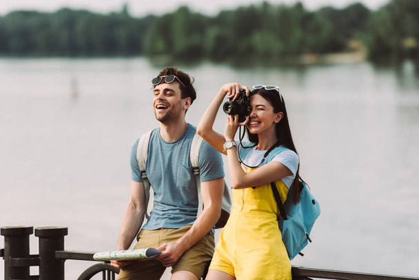 smiling and asian woman taking photo and handsome man holding map  - Foto, Bild