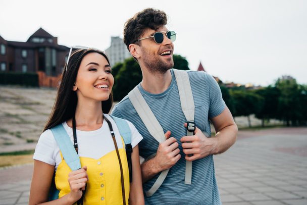 handsome man and asian woman with backpacks looking away  - Photo, Image