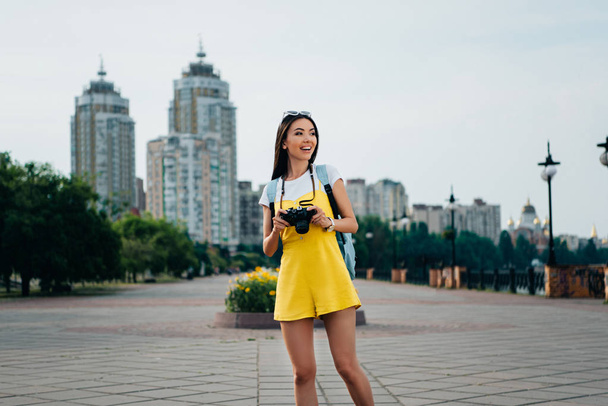 smiling and asian woman holding digital camera and looking away  - Foto, immagini