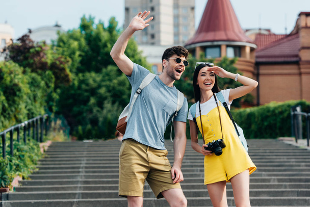 handsome man and asian woman with backpacks waving and looking away  - Photo, image