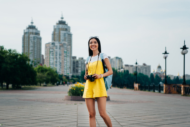 attractive and asian woman in overalls holding digital camera  - Foto, immagini