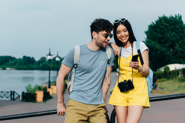 schöner Mann und asiatische Frau lächeln und schauen aufs Smartphone - Foto, Bild