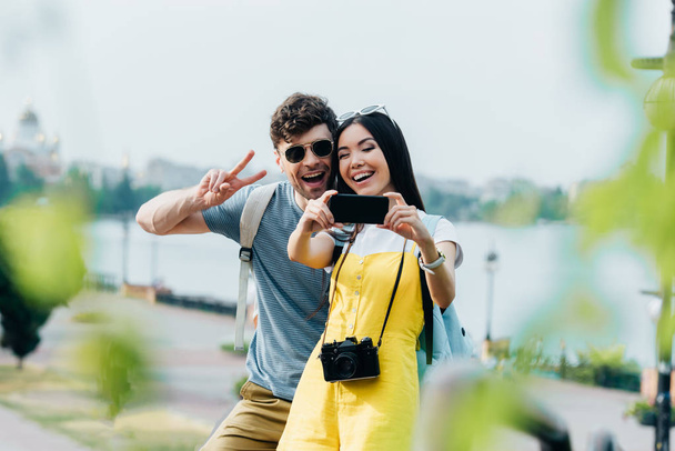 barış işareti gösteren yakışıklı adam ve selfie çeken Asyalı kadın  - Fotoğraf, Görsel
