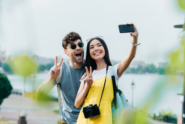 handsome man and asian woman showing peace signs and taking selfie  - Fotografie, Obrázek