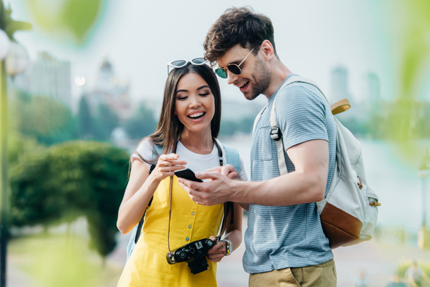 handsome man and asian woman smiling and looking at smartphone  - Foto, Imagem