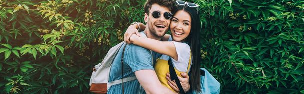panoramic shot of handsome man and asian woman hugging and looking at camera  - 写真・画像