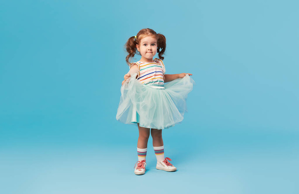 Little happy toddler child girl dreams of becoming ballerina in a cyan tutu skirt. Blue background. Space for text - Fotografie, Obrázek