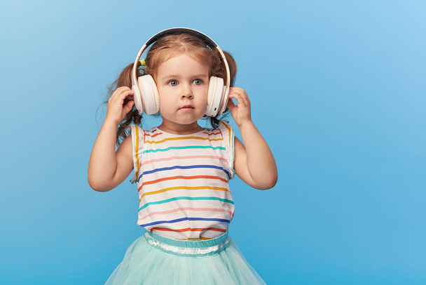 Happy smiling child enjoys listens to music in headphones over colorful bleu background. Vivid and fun emotions, happy child with pleasure listens to songs in wireless headphones - Foto, Bild
