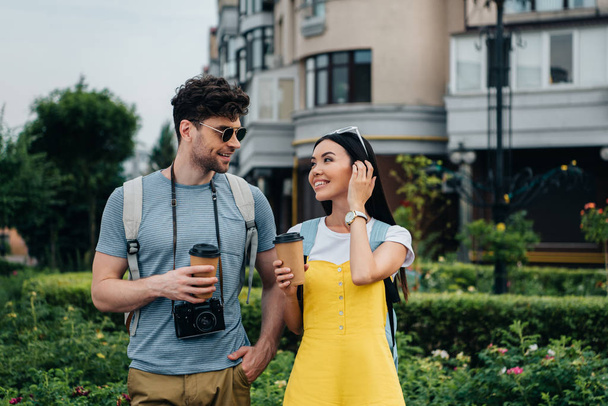 férfi a digitális fényképezőgép és az ázsiai nő beszél, és tartja papír csészék  - Fotó, kép