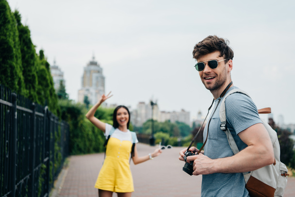 handsome man with digital camera and asian woman looking at camera  - Photo, Image