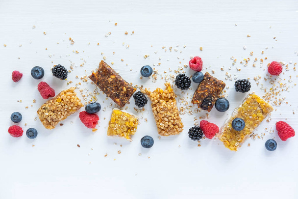 Frame for text with granola and natural berries of blueberries, raspberry, blackberry, blueberry and oatmeal on a white wooden background. Useful cereal bars for snacking and breakfast - Foto, afbeelding