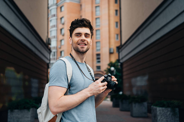handsome man in t-shirt holding digital camera and looking away  - Photo, Image