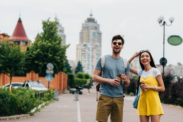 handsome man and asian woman smiling and holding paper cups  - Fotografie, Obrázek