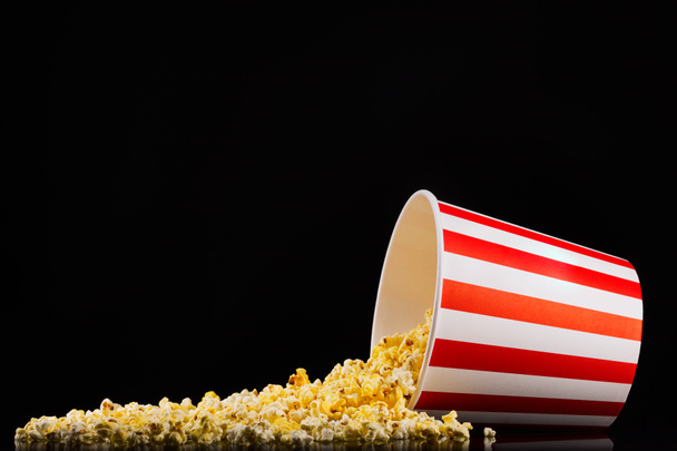 Scattered popcorn from paper striped bucket isolated on black background - Foto, imagen