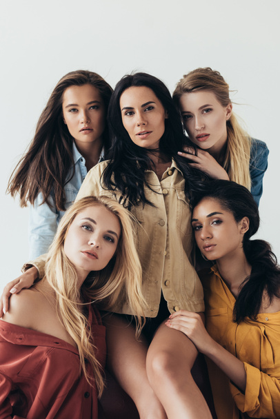 вид спереди пяти привлекательных мультиэтнических феминисток в разноцветных рубашках, обнимающих и смотрящих на камеру, изолированную на сером
 - Фото, изображение