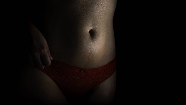 Belly of well shaped woman with erotic red panties on black background low key shot - Photo, Image