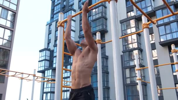 Muscular man doing pull-ups on horizontal bar. on workout area near house - Felvétel, videó