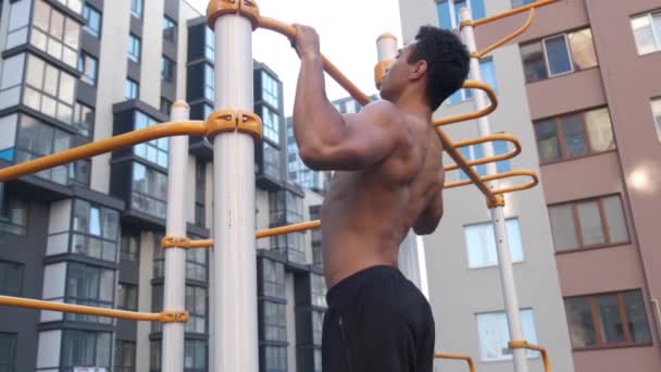 Muscular man doing pull-ups on horizontal bar. on workout area near house. - Imágenes, Vídeo