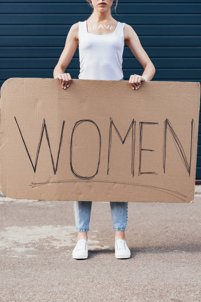 обрезанный вид феминистки со словом храбрый на теле держа плакат с надписью женщины на улице
 - Фото, изображение