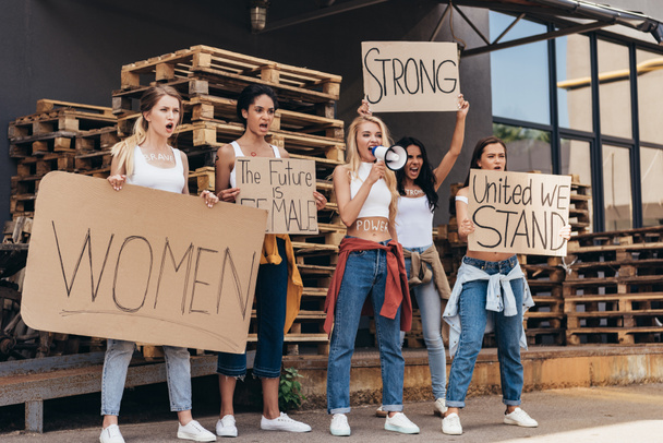 full length view of five screaming multiethnic feminists with loudspeaker holding placards with slogans on street - Foto, Imagem