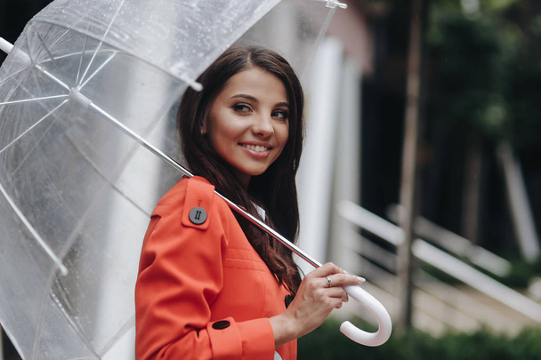 Modefoto von jungen Mädchen posiert mit Regenschirm. sie steht auf der Straße. Porträt einer jungen Frau im roten Mantel mit Regenschirm. - Foto, Bild