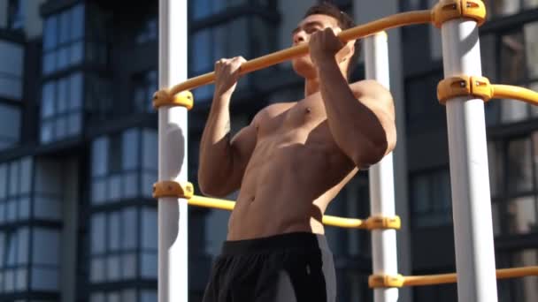 Muscular man doing pull-ups on horizontal bar. on workout area near house - 映像、動画