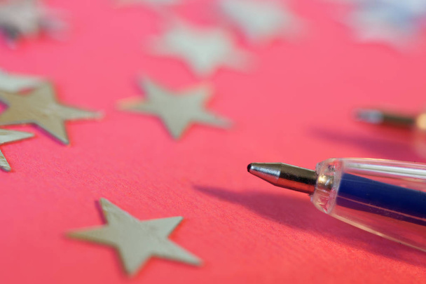 Una pluma azul se encuentra junto a las estrellas de plata sobre un fondo rosa. G
 - Foto, Imagen