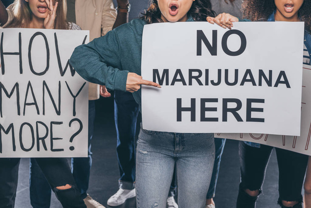 vista recortada de chica emocional señalando con el dedo en el cartel sin marihuana aquí letras cerca de personas multiculturales en negro
  - Foto, Imagen