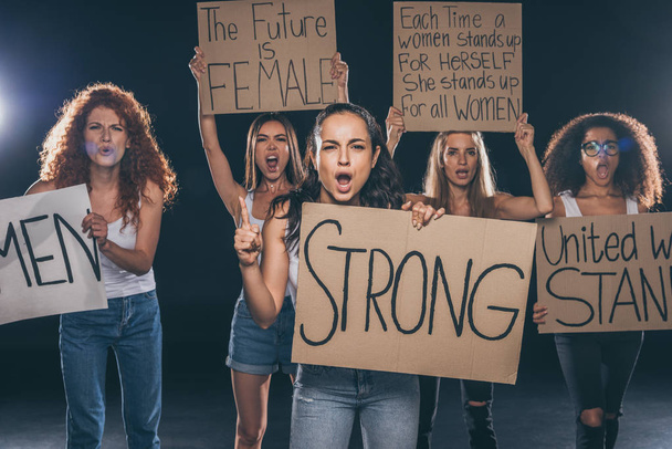 young and emotional multicultural women holding placards on black   - Фото, изображение