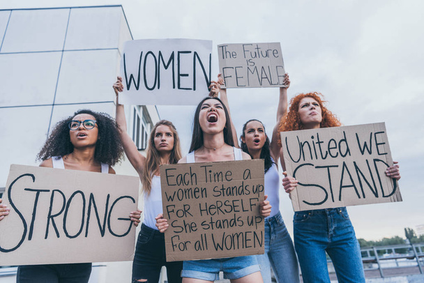 Blick auf multikulturelle Frauen, die Plakate hochhalten und draußen schreien  - Foto, Bild