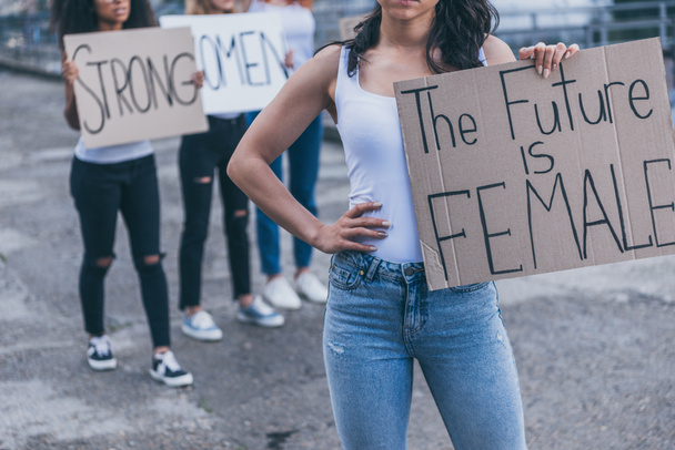 vista recortada de niña sosteniendo pancarta con el futuro es letras femeninas, mientras que de pie con la mano en la cadera
 - Foto, imagen