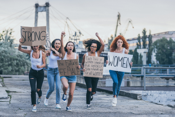 emotional multicultural women holding placards and running outside  - Foto, Bild