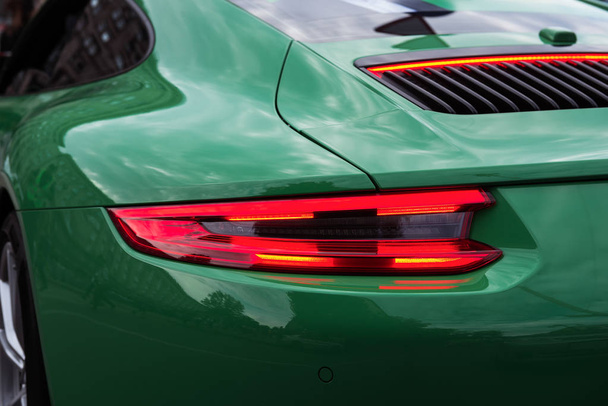 Zöld sportkocsi vörös háttérvilágítással on. Closeup egy luxus autó test. Modern LED-jelzőfény. Hátsó fénycsík. - Fotó, kép
