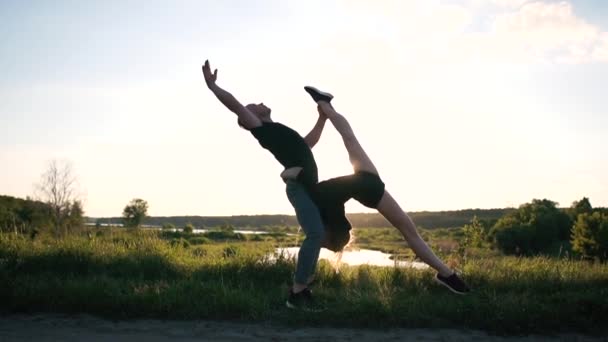 Umělecký blonďák stojí a nechává svou dívku, jak dělá přední nohu mezi nohama u jezera v slo-mo - Záběry, video