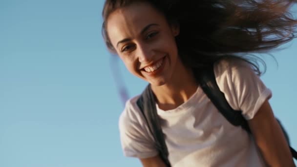 ευτυχισμένο χαρούμενο χαμογελαστή νεαρή όμορφη γυναίκα με λευκό t-shirt στέκεται στη γέφυρα στο γαλάζιο του ουρανού φόντο, γέλιο, απολαμβάνοντας το ειρηνικό ηλιοβασίλεμα και κοιτάζοντας την κάμερα. - Πλάνα, βίντεο