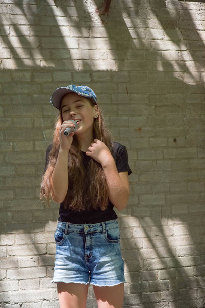 Krásná holčička s mikrofonem na cihlovou zeď pozadí - Fotografie, Obrázek